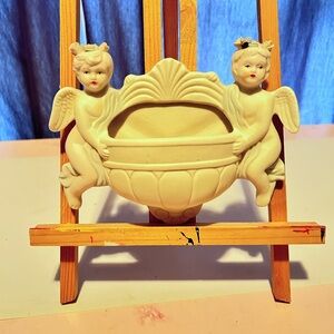 A vintage bisque wall pocket with two cherubs holding a central planter.